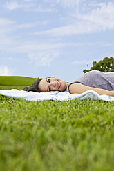 Eine junge Frau sonnt sich in der warmen Sonne und entspannt sich auf einer gemütlichen Decke inmitten der atemberaubenden Kulisse des bayerischen Parks - SKF000583