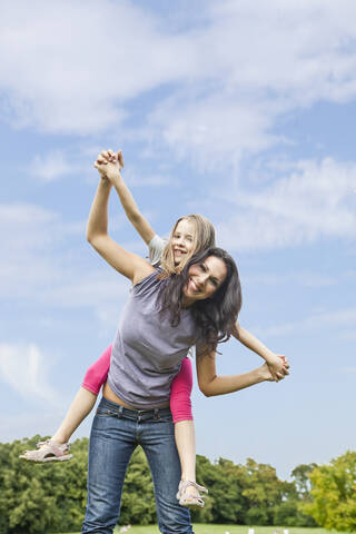 A joyful Bavarian mother carries her daughter on her back, radiating happiness in the park stock photo