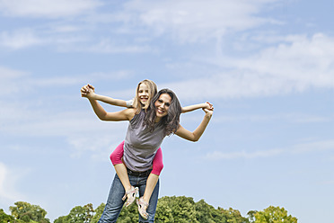 A joyful Bavarian mother carries her daughter on her back, posing for a portrait in the park with a smile - SKF000588