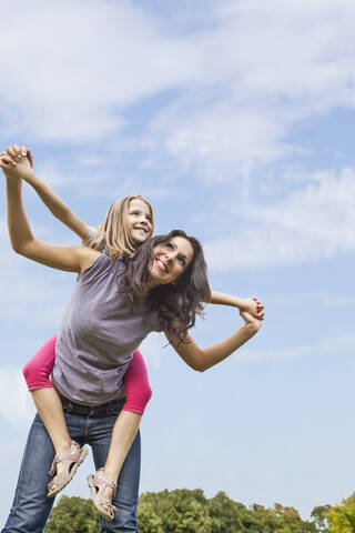 A joyful Bavarian mother carries her daughter on her back while enjoying a lovely day at the park stock photo