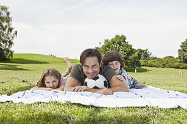Eine fröhliche bayerische Familie sonnt sich auf einer Picknickdecke und strahlt für ein Familienfoto - SKF000597