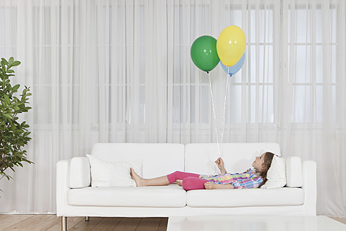 Ein junges Mädchen in München, Deutschland, ruht sich auf einer Couch aus und hält einen bunten Luftballon in der Hand - SKF000628