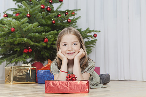 Ein junges Mädchen hält aufgeregt ein Geschenk vor einem schön geschmückten Weihnachtsbaum in München, Deutschland - SKF000631