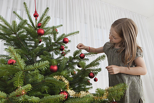 Ein junges Mädchen in München, Deutschland, schmückt einen Weihnachtsbaum mit festlichem Schmuck - SKF000632