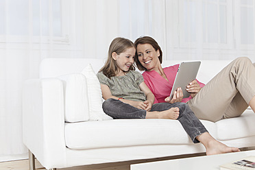 Eine glückliche Mutter und ihre Tochter in München, Deutschland, die sich über ein digitales Tablet mit einem breiten Lächeln im Gesicht unterhalten - SKF000649