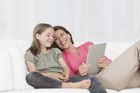 Eine glückliche Mutter und ihre Tochter in München, Deutschland, die sich über ein digitales Tablet unterhalten und ein Lächeln teilen, lizenzfreies Stockfoto