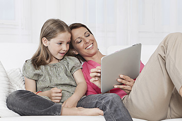 A happy mother and daughter in Munich, Germany, bonding over a digital tablet with smiles on their faces - SKF000651