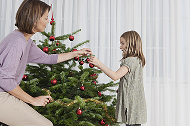 Eine Mutter und ihre Tochter in München, Deutschland, teilen einen besonderen Moment, während sie ihren Weihnachtsbaum schmücken - SKF000652
