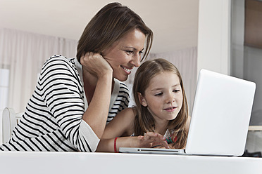 Eine glückliche Mutter und ihre Tochter in München, Deutschland, genießen es, ihren Laptop gemeinsam mit einem breiten Lächeln auf dem Gesicht zu benutzen - SKF000657