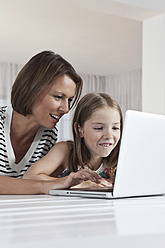 A happy mother and daughter in Munich, Germany, enjoy using their laptop together with smiles on their faces - SKF000658