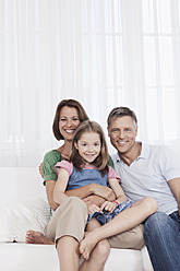 Eine glückliche Familie sitzt auf einer Couch in München, Deutschland, und posiert für ein Porträt mit einem breiten Lächeln auf ihren Gesichtern - SKF000676