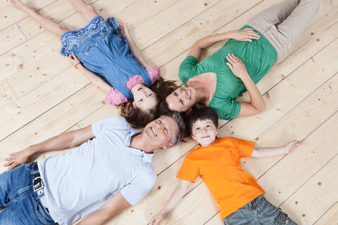 Familienzusammenführung in München, Deutschland: Eltern und Kinder lachen gemeinsam, während sie auf dem Boden liegen, lizenzfreies Stockfoto