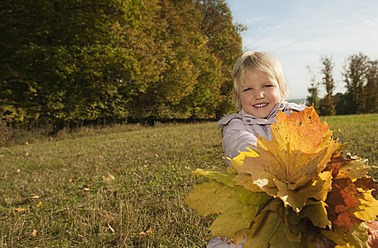 Ein fröhliches Mädchen aus Bayern hält Blätter und lächelt für ein Porträt in Deutschland - RNF000776