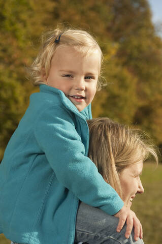 Eine glückliche Mutter in Bayern trägt ihre Tochter auf der Schulter, beide lächeln und genießen die gemeinsame Zeit, lizenzfreies Stockfoto