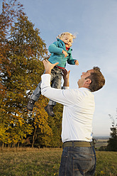 Ein Vater wirft seine Tochter freudig in die frische Herbstluft inmitten der malerischen bayerischen Landschaft in Deutschland - RNF000811