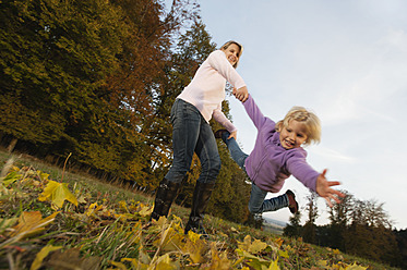 Eine Mutter und ihre Tochter genießen das bunte Herbstlaub beim Spielen in Bayern, Deutschland - RNF000814