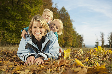 Germany, Bavaria, Family lying on leaves during autumn, smiling, portrait - RNF000816