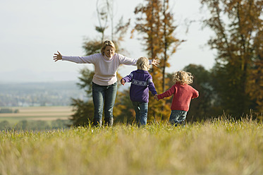 Familienzusammenführung auf einer malerischen bayerischen Wiese, während die Töchter mit ihrer Mutter im Hintergrund laufen - RNF000817