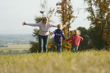 Family bonding in the picturesque Bavarian meadow as daughters run with their mother in the background - RNF000817