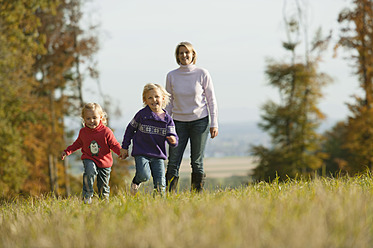 Family fun in Bavaria as daughters frolic in a meadow with their mother in the background - RNF000818