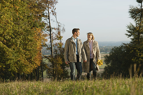 Ein Paar genießt die landschaftliche Schönheit Bayerns, Deutschland, bei einem gemütlichen Spaziergang durch das üppige grüne Gras - RNF000827