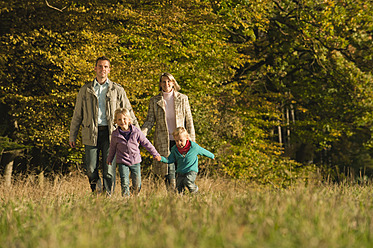 Eine Familie macht einen gemütlichen Spaziergang über eine schöne bayerische Wiese, umgeben von buntem Herbstlaub - RNF000830