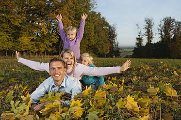 Eine fröhliche Familie sonnt sich in der Schönheit des bayerischen Herbstes, liegt auf einem Bett aus Blättern und posiert für ein Foto - RNF000834