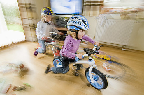 Germany, Bavaria, Girls playing with bicycle in living room - RNF000838