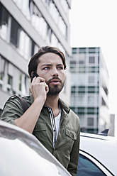 Deutschland, Köln, Junger Mann am Telefon neben Auto - FMKF000354