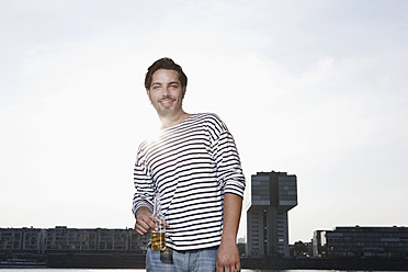 Germany, Cologne, Young man with beer bottle, smiling, portrait - FMKF000358