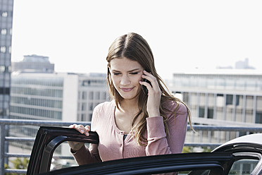 Deutschland, Köln, Junge Frau am Telefon in der Nähe eines Parkplatzes, lächelnd - FMKF000364
