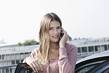 Deutschland, Köln, Junge Frau am Telefon in der Nähe des Parkplatzes, lächelnd, Porträt - FMKF000365
