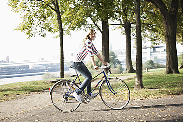 Germany, Cologne, Young woman on bicycle, smiling, portrait - FMKF000374
