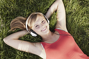 Germany, Cologne, Young woman lying in grass, smiling, portrait - FMKF000379