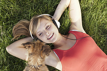 Germany, Cologne, Young woman with dog lying in grass, smiling - FMKF000380