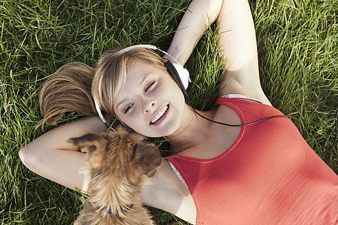 Deutschland, Köln, Junge Frau mit Hund im Gras liegend, lächelnd - FMKF000380