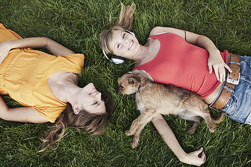 Deutschland, Köln, Junge Frau liegt mit Hund im Gras, lächelnd - FMKF000414