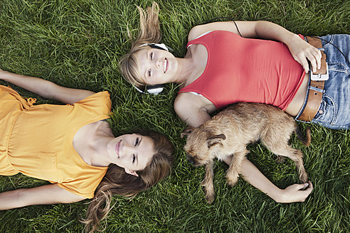Deutschland, Köln, Junge Frau im Gras liegend mit Hund, lächelnd, Porträt - FMKF000415