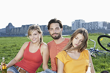 Deutschland, Köln, Junger Mann und Frau mit Bierflasche im Gras, lächelnd - FMKF000433