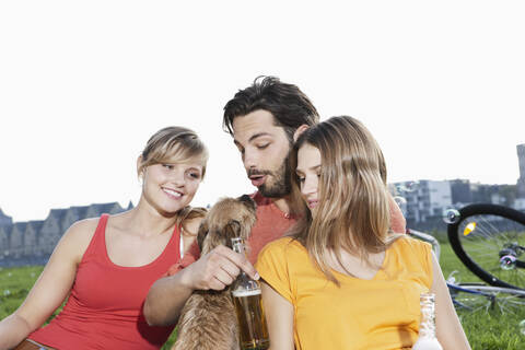 Deutschland, Köln, Junger Mann und Frau mit Hund und Bierflasche im Gras, lächelnd, lizenzfreies Stockfoto