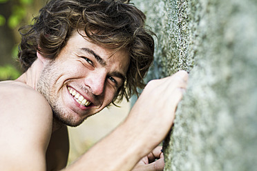 Thailand, Koh Tao, Junger Mann klettert auf Felsen, lächelnd, Porträt - MBEF000209