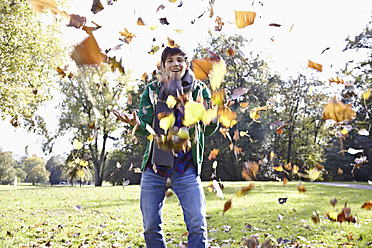 Germany, Cologne, Young man playing with leaves in park, smiling, portrait - RHF000004