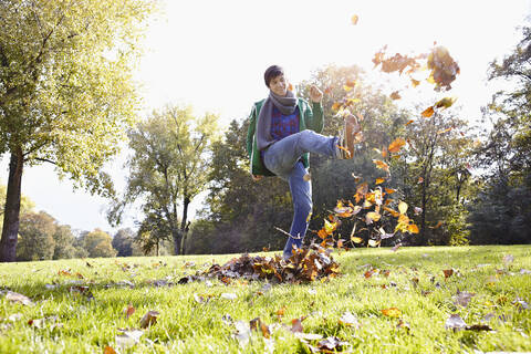 Deutschland, Köln, Junger Mann spielt mit Blättern im Park, lächelnd, lizenzfreies Stockfoto