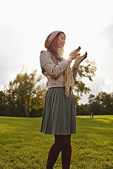 Deutschland, Köln, Junge Frau mit Handy im Park - RHF000007