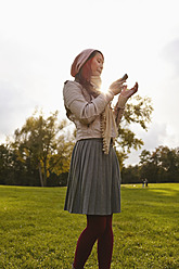 Germany, Cologne, Young woman with cell phone in park - RHF000007