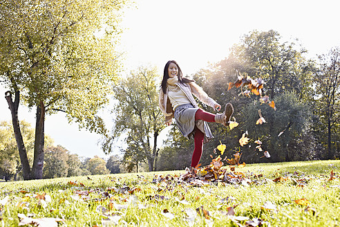 Deutschland, Köln, Junge Frau spielt im Park mit Blättern, lächelnd - RHF000010