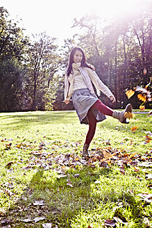 Germany, Cologne, Young woman playing in park with leaves, smiling - RHF000011