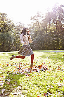 Germany, Cologne, Young woman playing in park with leaves - RHF000012