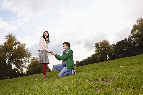 Deutschland, Köln, Junger Mann macht Frau im Park einen Heiratsantrag, lächelnd - RHF000021