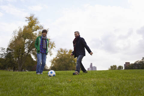 Deutschland, Köln, Mann spielt Fußball im Park, lächelnd, lizenzfreies Stockfoto